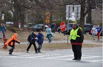 School crossing guard in the middle of the street with a stop sign, children crossing the road